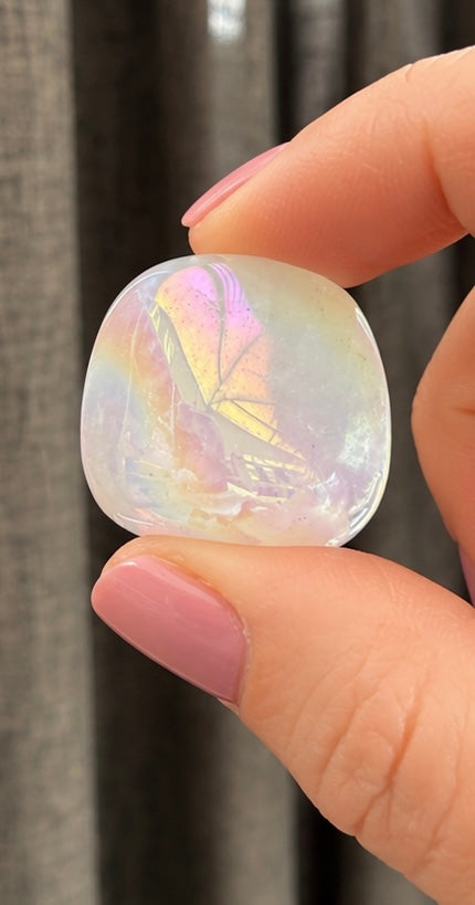 Actual iridescent aura quartz tumble held between fingers