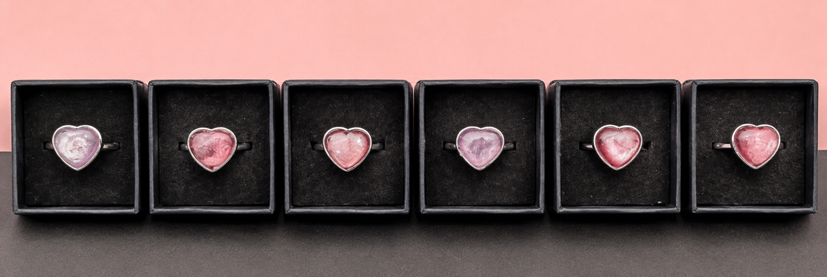 Illustrative group image showing pink and lilac lepidolite heart rings in black boxes; natural stones vary