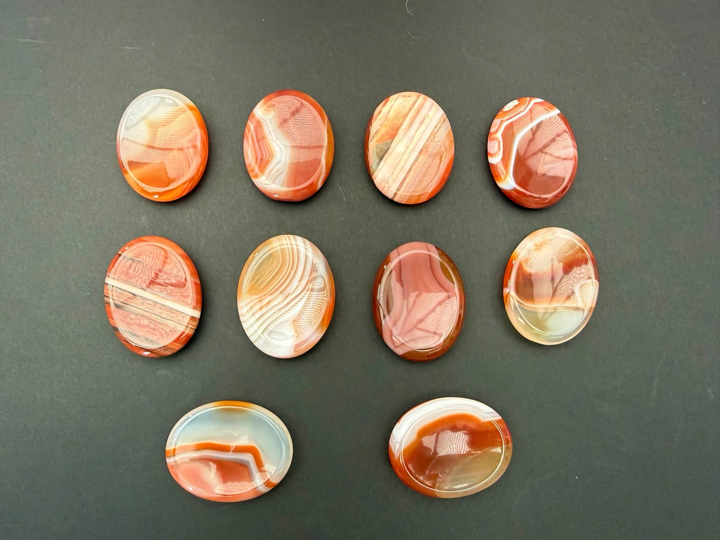 Ten polished Banded Carnelian worry stones showing natural orange and cream banding